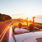 Happy Couple Driving on Country Road into the Sunset in Classic Vintage Sports Car